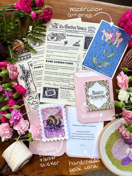 Collection of handmade items including cards, stickers, and a book card on a wooden surface with flowers.
